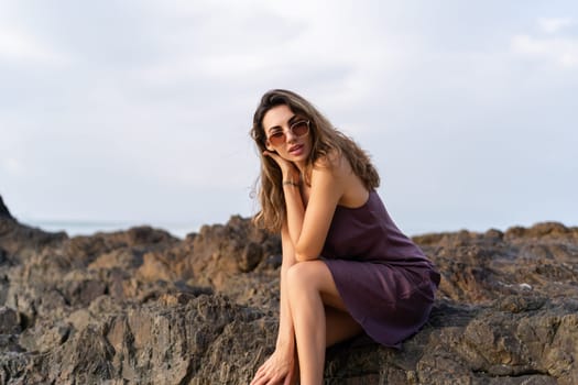 Stylish romantic tender sensual woman in silk dress and sunglasses on the beach at sunset