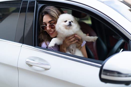 A happy woman and a dog in a car on a summer trip. Cute pomeranian spitz. Vacation with a pet.