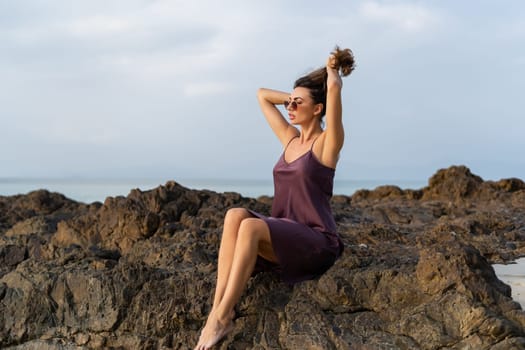 Stylish romantic tender sensual woman in silk dress and sunglasses on the beach at sunset