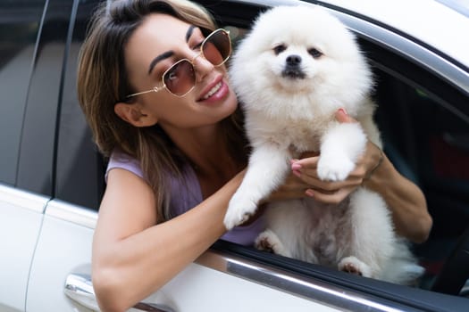 A happy woman and a dog in a car on a summer trip. Cute pomeranian spitz. Vacation with a pet.