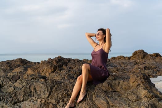 Stylish romantic tender sensual woman in silk dress and sunglasses on the beach at sunset