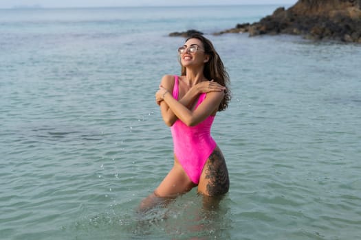 Stylish romantic tender, athletic body good shape, slim sensual woman in a pink swimsuit and sunglasses on the beach at sunset