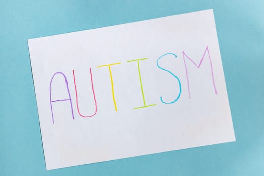 Text word autism on paper sheet written by colorful letter, on blue background