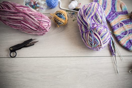 Colored threads, knitting needles and other items for hand knitting, on a light wooden table .