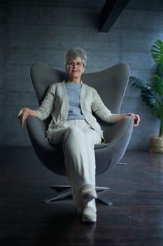 attractive middle aged smiling woman model sitting in chair looking at camera at office