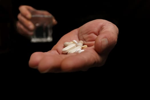 man with pills in one hand and a glass of water in the other isolated on black background