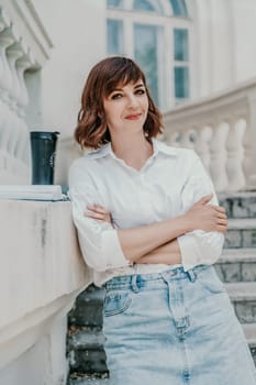 Woman building city. A business woman in a white shirt and denim skirt stands leaning against the wall on the steps of an ancient building in the city.