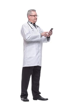 Closeup photo of man doctor standing isolated on white background looking attentively at screen of cellphone, smiling nicely
