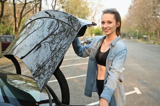 Portrait of smiling caucasian woman in a sporty outfit standing near her car while going to the gym. Fitness lifestyle concept.