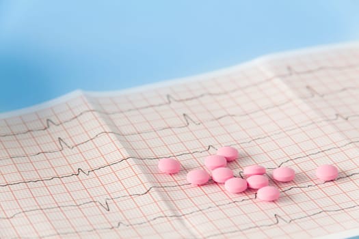 A large handful of pink pills lie on the electrocardiogram of the heart on a blue background. The concept of a healthy lifestyle and timely medical examination