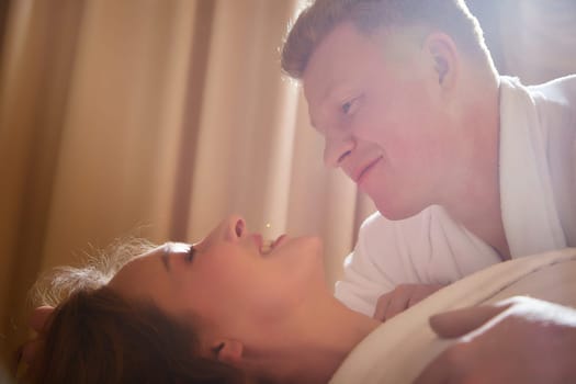 An adult couple of newlyweds in in white robes in a hotel room after the wedding. A guy and a girl, a man and a woman in beautiful room. The concept of hugs, love and care