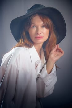 Portrait of a young sexy girl in white shirt and hat on a grey background. Classic style. dramatic portrait