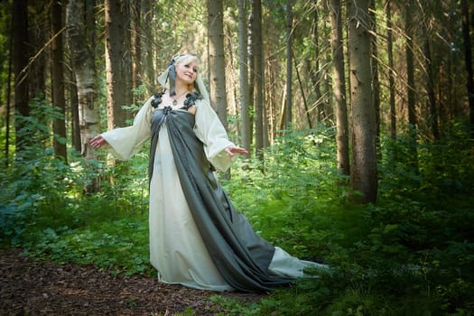 Adult mature woman 40-60 in a green long fairy dress in forest. Photo shoot in style of dryad and queen of nature. Fairy in beautiful green summer forest. Concept of caring for nature