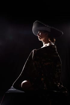 The silhouette of a girl in a veil looking like a statue or sculpture on black background. A model poses for a photo shoot in the studio