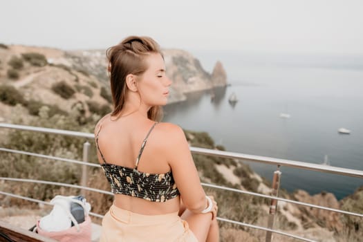 Woman travel sea. Happy tourist taking picture outdoors for memories. Woman traveler looks at the edge of the cliff on the sea bay of mountains, sharing travel adventure journey.