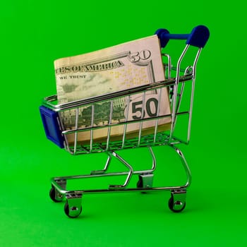 Shopping cart with 50 dollar bills on a green background. Shopping cart with 50 dollar bills on a green background close-up.