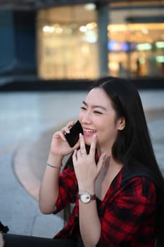 Happy Asian woman sitting in the city street at night and talking on mobile phone.