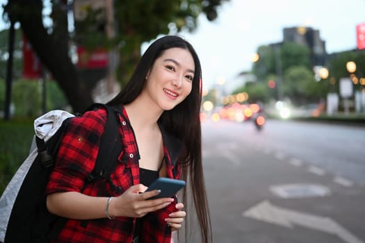 Female traveler using smart phone waiting taxi in evening street.