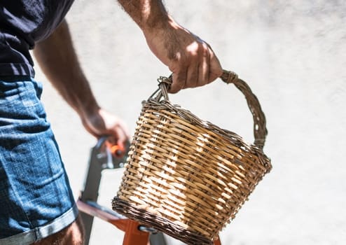 Hand holding wicker basket on light wall background.