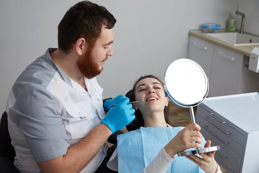 Young Woman Looking At Mirror With Smile In Dentist Office