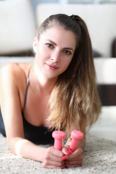 Portrait of beautiful young woman lies on floor with dumbbells. Home fitness and health concept