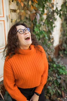 Portrait of carefree young woman smiling with urban background. Cheerful latin girl wearing eyeglasses in the city. Happy brunette woman with curly hair spectacles smiling.