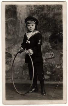 GERMANY - CIRCA 1920: Vintage photo shows boy wears sailor costume with hoop. Antique black white photo.