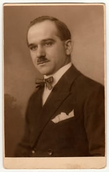 PRAGUE, THE CZECHOSLOVAK REPUBLIC - 1925: Vintage studio portrait shows man wears jacket and bow tie. Antique black white photo with sepia tint.