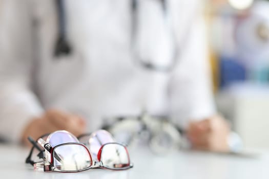 Ophthalmologist sits in background with various glasses for fitting lenses in frame. Treatment of farsightedness myopia and astigmatism