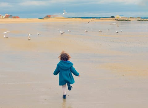 Girl in a green coat run away. Seagulls flying around at a Atlantic ocean