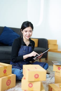 Startup small business entrepreneur of freelance Asian woman smiling and using tablet computer with Cheerful success of item online marketing packaging box and delivery SME idea concept.