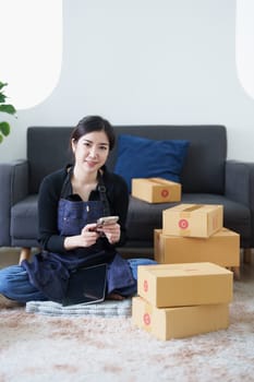Startup small business entrepreneur of freelance Asian woman smiling and using smart phone mobile with Cheerful success of item online marketing packaging box and delivery SME idea concept.