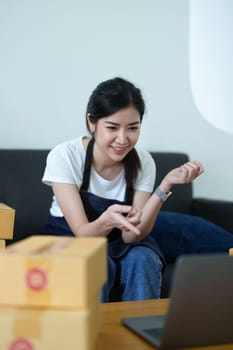 Starting small business entrepreneur of independent Asian woman smiling using laptop computer with cheerful success of online marketing package box items and SME delivery concept.