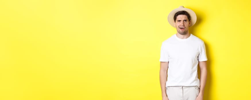 Concept of tourism and summer. Confused guy traveller in straw hat, looking puzzled, cant understand something, standing over yellow background.