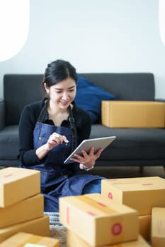 Startup small business entrepreneur of freelance Asian woman smiling and using tablet computer with Cheerful success of item online marketing packaging box and delivery SME idea concept.