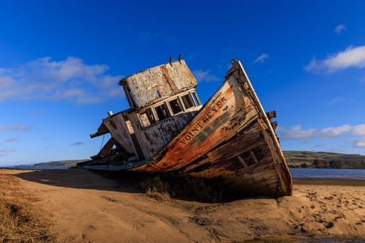Historic wooden fishing boat wreck on sandy beach in sun and blue sky. High quality photo