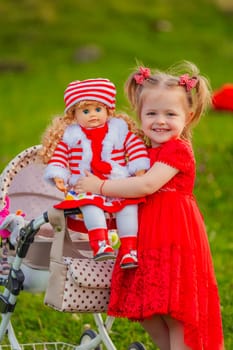 The girl plays with a doll in nature, holding her in her arms