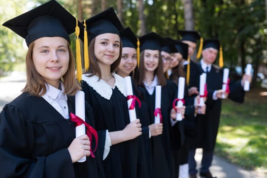 Row of young people in graduation gowns outdoors. Age student