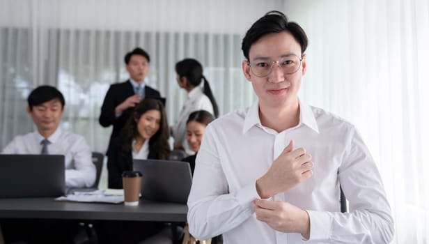 Portrait of focus young successful confident male manager, executive wearing business wear in harmony office arm crossed with blurred meeting background of colleagues, office worker.