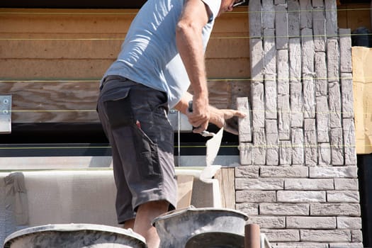 the bricklayer makes the facade of the house from gray bricks with cement and plaster at the construction site. High quality photo