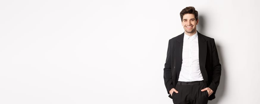 Image of handsome caucasian man in party suit, smiling pleased, attend formal event, standing over white background.