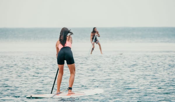 Sea woman and man on sup. Silhouette of happy young woman and man, surfing on SUP board, confident paddling through water surface. Idyllic sunset. Active lifestyle at sea or river