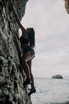 A girl climbs a rock. The athlete trains in nature. Woman overcomes difficult climbing route. Extreme hobby. Tourist woman rock climber hiking on mountains rocks over beautiful sea coast