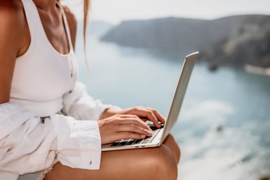 Digital nomad, Business woman working on laptop by the sea. Pretty lady typing on computer by the sea at sunset, makes a business transaction online from a distance. Freelance remote work on vacation