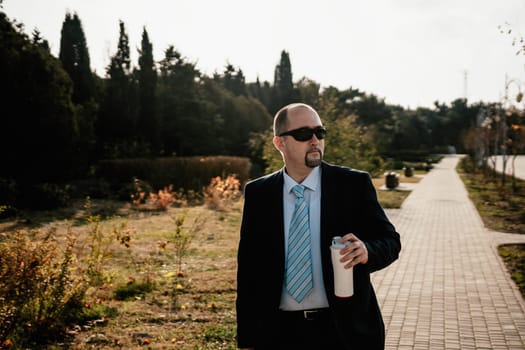 Mature entrepreneur drink coffee in autumn park. Senior executive rest in city park.