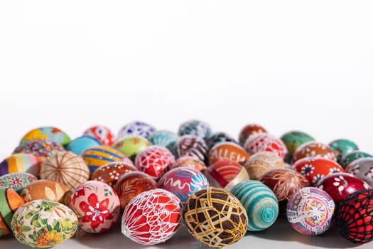 Easter eggs made in different technologies and arranged on a white background in rather random places. A large number of colorful eggs lying side by side.