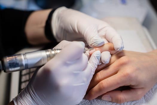 The beautician performs the preparation of the nail plate for further nail care. Using a nail milling machine in a beauty salon. Professional equipment for performing beauty treatments.