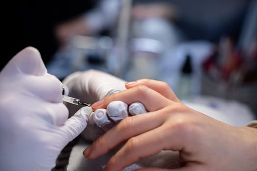 Close-up of the hands of a beauty salon client. The beautician applies a base coat to the client's nails. Preparing the nail plate for further cosmetic procedures.
