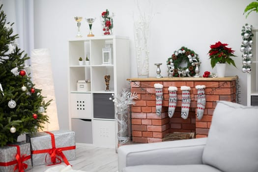 A bright living room with a fireplace. Live Christmas tree decorated in white and red. Silver gifts with red ribbons.