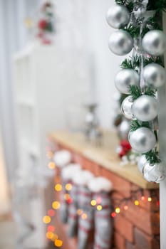 Silver baubles on spruce twigs and decorated fireplace in background.